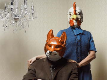 A couple wearing a chicken and a fox mask.