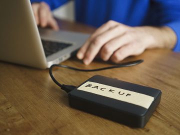 An external storage device that has the label "backup" is connected to a Macbook computer