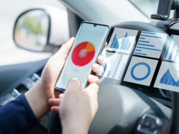 A phone showing multiple data streams is being viewed within the front seat of a car.