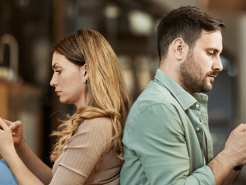 A man and a woman with their backs to each other looking at their phones