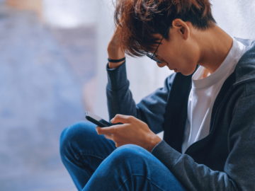 A young man sat down with his head in one hand and holding a phone in the other.