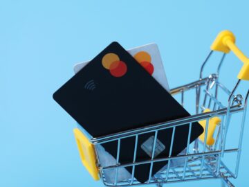 A tiny shopping cart carries two credit cards. It rests in front of a light blue background.