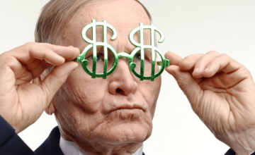 An older man holding dollar sign glasses up to his eyes.