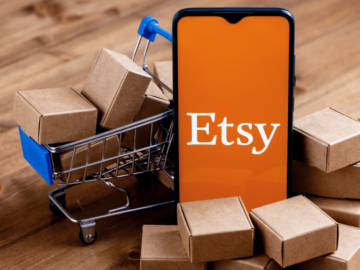 Image of a phone with an Etsy logo on it in front of boxes and a shopping trolley