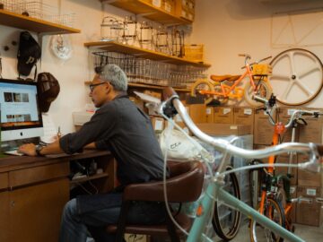 A man manages his online web business as he sits amongst his inventory of bicycles and accessories