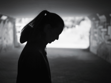 Silhouette of woman in underpass looking down at the ground