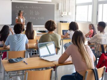 A group of students looking toward a teacher at the front of a classroom
