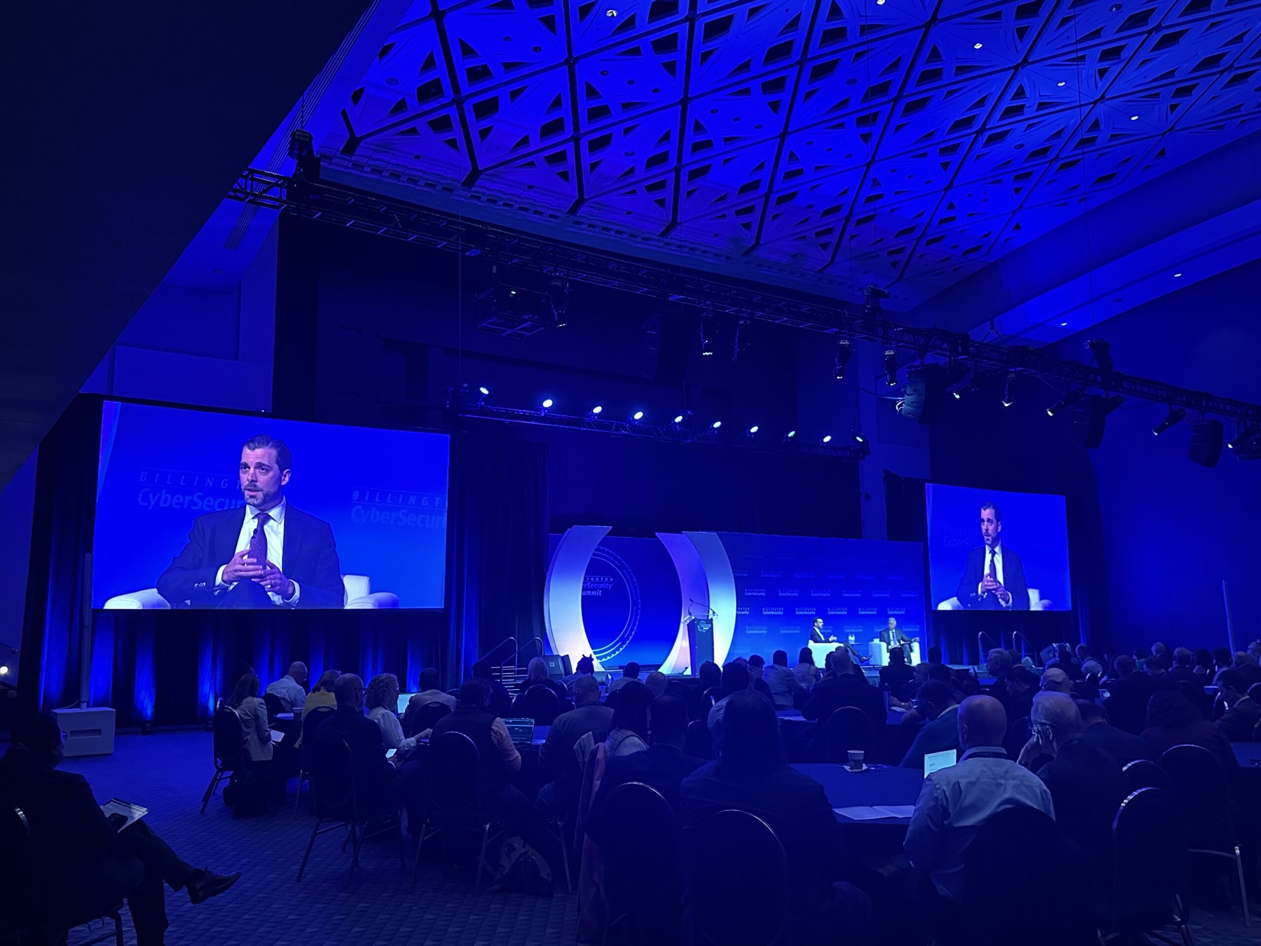 Acting federal cyber chief outlines his three priorities for the next year Michael Duffy is pictured speaking onstage in a room at the Washington Convention Center. The stage is illuminated in a deep blue light and he is visible via a livestream on two large screens that flank the stage.